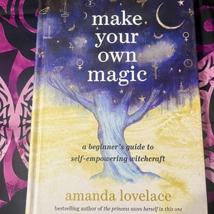 May include: A hardcover book titled "make your own magic" with a blue and gold celestial design. The cover features a tree illustration and the author's name, Amanda Lovelace. The book is a beginner's guide to self-empowering witchcraft.