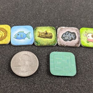 May include: A set of six colorful game tiles with various images, including a leaf, a fish, a tree trunk, a rock, a cow, and a green tile with a pattern.