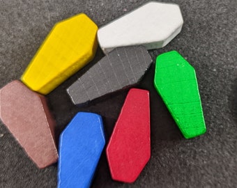 May include: Seven wooden coffin-shaped game pieces in different colours: yellow, white, black, green, brown, blue, and red. The pieces are about the size of a UK 20 pence coin.