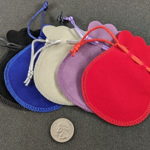 May include: Five velvet drawstring pouches in different colors: black, blue, beige, purple, and red. The pouches are lined up in a row, with the red pouch at the front. The pouches are about the size of a quarter.