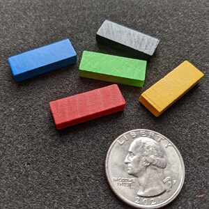May include: Five wooden rectangular blocks in different colors: blue, green, red, yellow, and black. The blocks are arranged in a semi-circle on a black surface. A silver US quarter is in the lower right corner of the image.