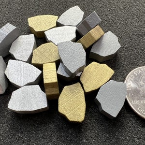 Könnte beinhalten: Eine Sammlung kleiner, unregelmäßig geformter Metallstücke in Silber- und Goldtönen. Die Stücke haben eine strukturierte Oberfläche und sind auf einem dunklen Hintergrund verstreut. Eine US-Vierteldollarmünze ist zum Größenvergleich enthalten.