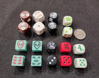 May include: A collection of novelty dice with various designs, including skulls, aliens, and cannabis leaves. The dice are in various colors, including brown, black, white, red, and green. A quarter is included for size comparison.