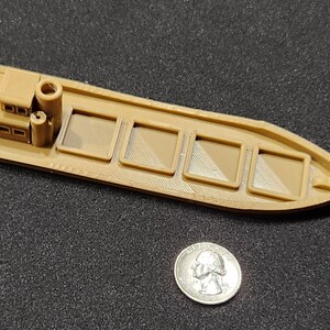 May include: A brown plastic model of a small boat with a cabin and four cargo holds. The boat is approximately 10 cm long.