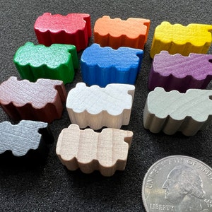Könnte beinhalten: Elf farbige Holzspielsteine in Form stilisierter Züge. Die Farben umfassen Rot, Orange, Gelb, Grün, Blau, Lila, Braun, Weiß, Grau und Schwarz. Eine amerikanische Vierteldollarmünze dient als Größenvergleich.