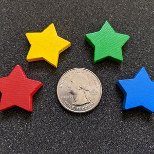 Könnte beinhalten: Vier Holzsterne in den Farben Rot, Gelb, Grün und Blau, angeordnet um eine US-amerikanische 25-Cent-Münze. Die Münze befindet sich in der Mitte des Bildes und die Sterne sind um die Münze herum angeordnet.