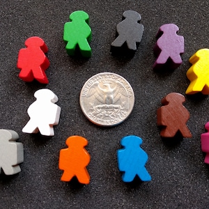 Pode incluir: Um conjunto de 10 peças de jogo de madeira em várias cores, incluindo vermelho, verde, azul, amarelo, roxo, marrom, branco, cinza, laranja e rosa. As peças têm a forma de pessoas e estão dispostas em um círculo em torno de uma moeda de um quarto de dólar americano de prata.