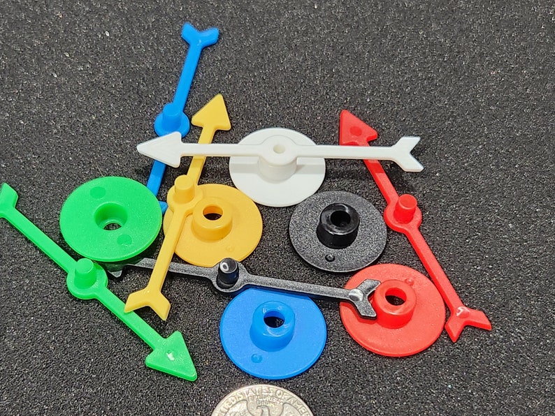 May include: A set of colorful plastic game pieces with arrows and circular bases. The pieces are in various colors, including green, yellow, blue, red, white, and black.