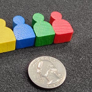 May include: Four brightly coloured wooden game pieces in yellow, blue, green, and red, arranged in a row. A coin is in the foreground for size comparison. The pieces are approximately 2 cm tall.