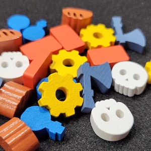 May include: A selection of brightly coloured wooden game pieces, including yellow cogs, orange rectangles, blue axes, and white skull shapes. Other shapes include blue keys and orange bread-like pieces. The pieces are scattered on a dark surface.