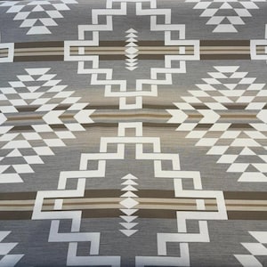 May include: A gray fabric with a geometric pattern in white and brown. The design features diamond and zigzag shapes, creating a Southwestern or Native American aesthetic. The fabric is likely used for blankets or upholstery.