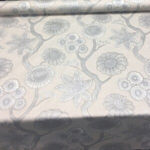 Puede incluir: Tela blanca con un patr&oacute;n floral plateado. El patr&oacute;n presenta flores y hojas estilizadas.
