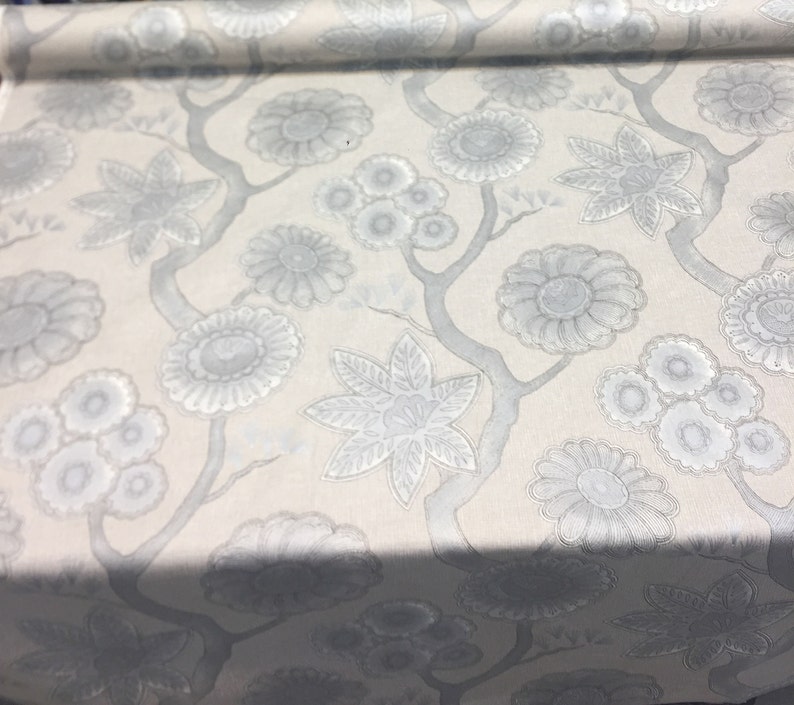 Puede incluir: Tela blanca con un patr&oacute;n floral plateado. El patr&oacute;n presenta flores y hojas estilizadas.