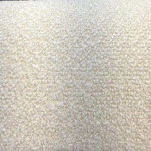 Könnte beinhalten: Nahaufnahme eines cremefarbenen, strukturierten Stoffes. Das Material hat eine geschlungene, noppige Oberfläche, die ein weiches, taktiles Aussehen erzeugt. Die neutrale Farbe und Textur deuten auf ein gemütliches Textil hin, das für Polster oder Heimdekoration geeignet ist.