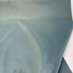 May include: A smooth, light blue fabric with a subtle sheen. The fabric is folded in half, showing the texture and color.