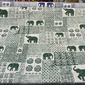 May include: Green and white fabric with a repeating pattern of elephants and geometric shapes. The fabric has a patchwork design with different patterns in each square.
