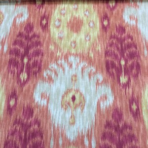 May include: A close-up of a fabric with an ikat pattern in shades of pink, orange, and beige. The fabric has a subtle sheen and a soft texture.