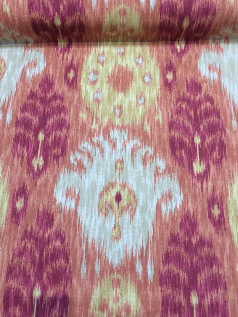 May include: A close-up of a fabric with an ikat pattern in shades of pink, orange, and beige. The fabric has a subtle sheen and a soft texture.