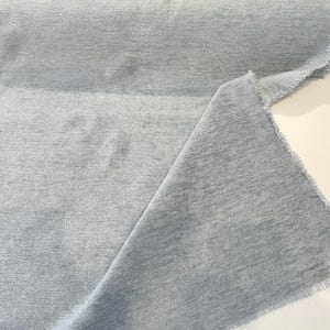 May include: Close-up of a light blue fabric with a textured, woven appearance. The fabric has a slightly frayed edge.