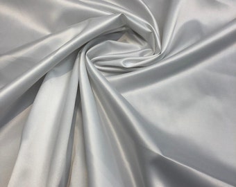 May include: White satin fabric with a smooth, silky texture. The fabric is draped and folded, creating soft curves and folds.