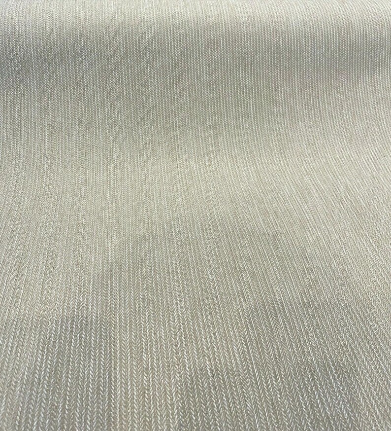 Puede incluir: Primer plano de una tela beige con un sutil patr&oacute;n de espiga blanca. La tela tiene una textura lisa y una superficie ligeramente texturizada.
