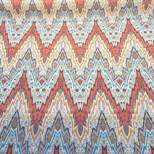 May include: A fabric with a repeating zigzag pattern in shades of coral, blue, yellow, and gray. The design incorporates floral and geometric elements, creating a vibrant and textured appearance. The fabric appears to be a woven material.
