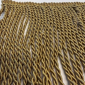 May include: Gold twisted fringe trim. The fringe is made of a soft, woven material and has a subtle sheen.