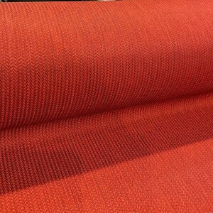 May include: Close-up of a red fabric with a herringbone pattern. The fabric is rolled up and the texture is visible.