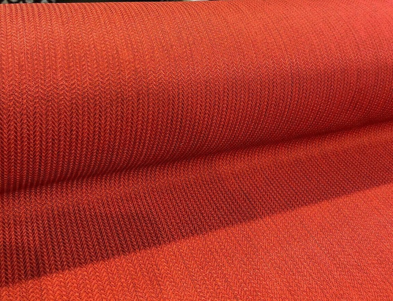 May include: Close-up of a red fabric with a herringbone pattern. The fabric is rolled up and the texture is visible.