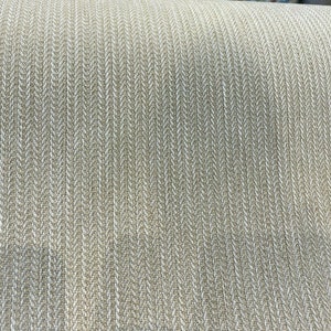 Puede incluir: Primer plano de una tela beige con un patr&oacute;n de espiga blanco. La tela tiene una textura sutil y una sensaci&oacute;n ligeramente rugosa.