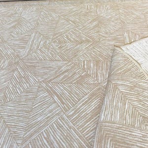 Könnte beinhalten: Beigefarbener Stoff mit einem weißen geometrischen Muster aus diagonalen Linien, die Rauten bilden.