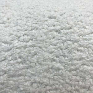 May include: Close-up of a white fluffy fabric with a soft, textured surface. The fabric has a fuzzy, sheepskin-like appearance.