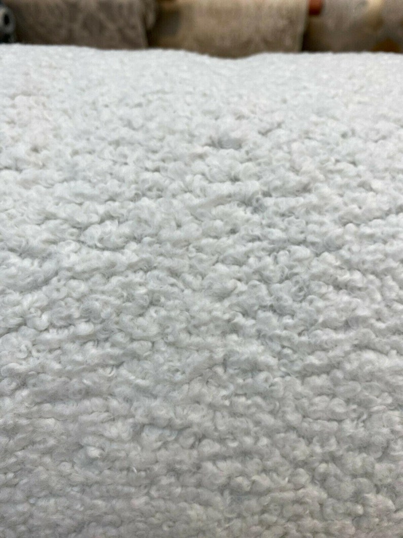 May include: Close-up of a white fluffy fabric with a soft, textured surface. The fabric has a fuzzy, sheepskin-like appearance.