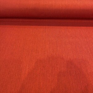 May include: Close-up of a red fabric with a textured woven pattern. The fabric has a subtle herringbone design.