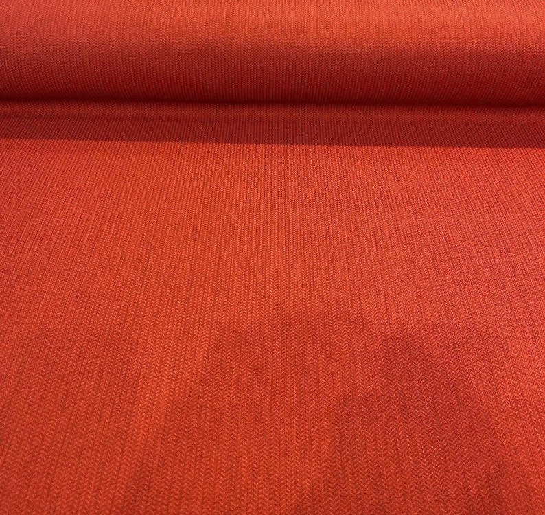 May include: Close-up of a red fabric with a textured woven pattern. The fabric has a subtle herringbone design.