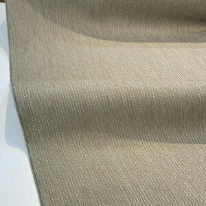 Puede incluir: Primer plano de una tela beige con un sutil patr&oacute;n de espiga. La tela tiene una superficie ligeramente texturizada y un aspecto suave y natural.