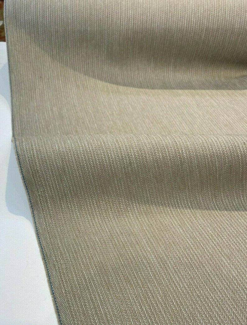 Puede incluir: Primer plano de una tela beige con un sutil patr&oacute;n de espiga. La tela tiene una superficie ligeramente texturizada y un aspecto suave y natural.