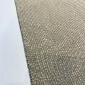 Puede incluir: Primer plano de una tela beige con un patr&oacute;n de espiga. La tela tiene un brillo sutil y una superficie ligeramente texturizada.