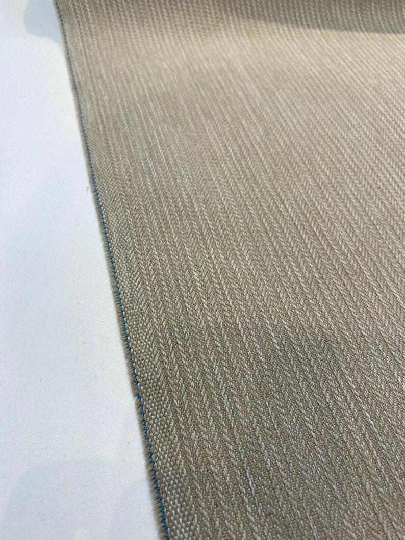 Puede incluir: Primer plano de una tela beige con un patr&oacute;n de espiga. La tela tiene un brillo sutil y una superficie ligeramente texturizada.