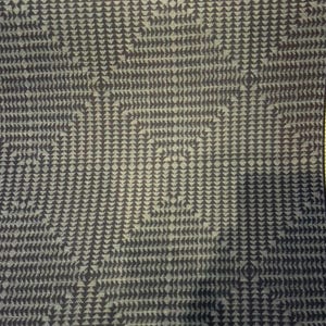May include: Close-up of a fabric with a repeating pattern of small, dark blue triangles on a lighter blue background. The triangles are arranged in rows and columns, creating a textured appearance. The pattern forms squares and diamond shapes.