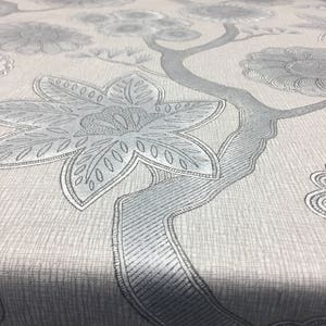 Puede incluir: Primer plano de una tela gris claro con un patr&oacute;n floral plateado. La tela tiene una textura sutil y presenta un dise&ntilde;o repetitivo de flores y ramas estilizadas.