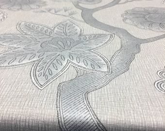 May include: A close-up of a light gray fabric with a silver floral pattern. The fabric has a subtle texture and features a repeating design of stylized flowers and branches.