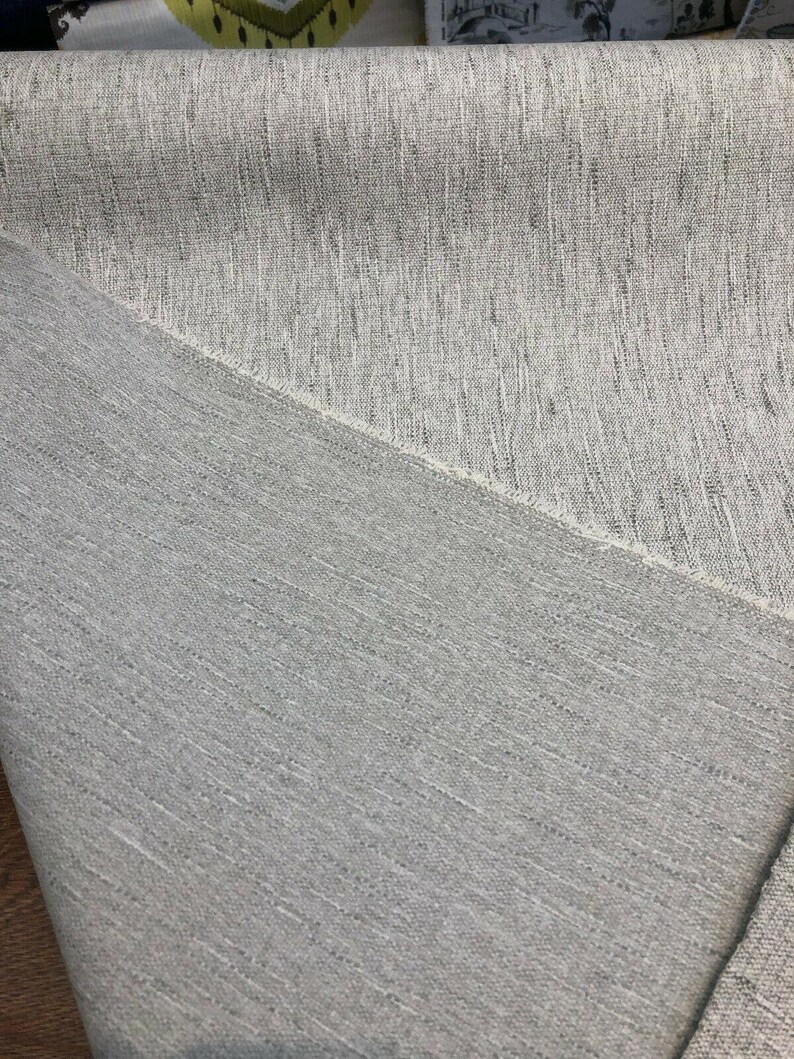 May include: Close-up of a light gray fabric with a subtle textured pattern. The fabric has a slightly rough feel and a woven appearance.