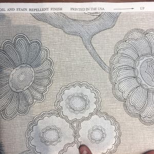 Puede incluir: Primer plano de una tela con un patr&oacute;n floral. La tela es gris claro con una textura sutil. Las flores est&aacute;n delineadas en negro y tienen un dise&ntilde;o delicado e intrincado. El texto "SOIL AND STAIN REPELLENT FINISH" y "PRINTED IN THE USA" es visible en la parte superior de la imagen.