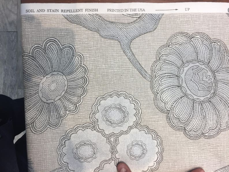 Puede incluir: Primer plano de una tela con un patr&oacute;n floral. La tela es gris claro con una textura sutil. Las flores est&aacute;n delineadas en negro y tienen un dise&ntilde;o delicado e intrincado. El texto "SOIL AND STAIN REPELLENT FINISH" y "PRINTED IN THE USA" es visible en la parte superior de la imagen.