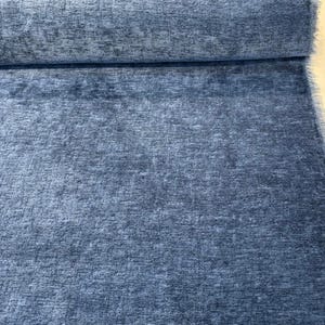 May include: A roll of blue fabric with a textured surface. The fabric has a soft, plush appearance and a subtle colour variation, creating a visual depth. The material appears suitable for upholstery or other textile projects.