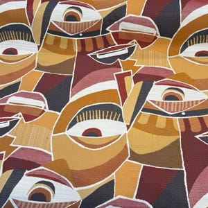May include: Abstract fabric with a repeating pattern of stylized faces in shades of brown, tan, and burgundy. The design features geometric shapes and lines, with white accents outlining the forms. The fabric has a textured appearance.
