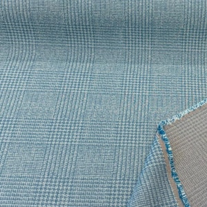 May include: Close-up of a light blue fabric with a classic glen plaid pattern. The fabric has a woven texture with a subtle white grid design. The reverse side of the fabric is a light gray color.