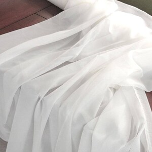 May include: White sheer fabric, soft and delicate, draped in folds. The fabric is lightweight and translucent, with a smooth texture.