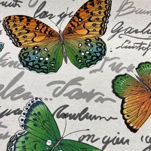 May include: A white fabric with a repeating pattern of butterflies. The butterflies are green, orange, and blue with black markings. The fabric has a gray script pattern that says "love you" and "autumn".